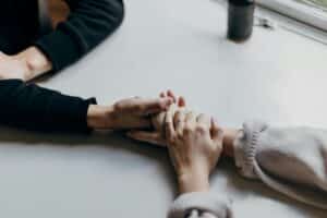 Two people are holding hands across a table, symbolizing support and connection. The soft lighting creates a calm and intimate atmosphere.